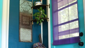 Una habitación con paredes color turquesa, un ventanal con marco morado, una cesta de mimbre con esteras y una planta colgante.