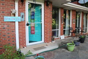 Una casa de ladrillo con una puerta turquesa, un letrero que dice 'Peace Love Joy' y plantas en macetas en el porche.