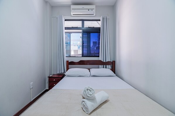 Une chambre d’hôtel comprenant un lit, une table de chevet, une fenêtre avec des rideaux et un appareil de climatisation.