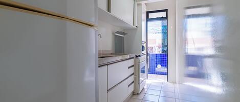 A kitchen with white cabinets, a stove, and a tiled floor.