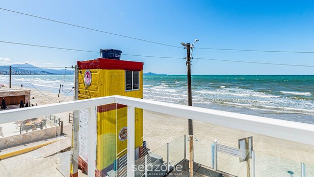 A yellow and red building with a sign, overlooking a beach with waves. - Duplex 3Q pé na areia c/ vista deslumbrante RAT001 (Porto Belo)