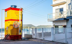 Um farol amarelo e vermelho com um emblema circular, próximo a um edifício moderno com varanda com vista para o mar.