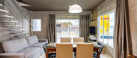 A modern living room with a sofa, dining table, chairs, and a staircase.