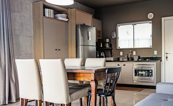Uma cozinha moderna com área de jantar, incluindo uma mesa com cadeiras, geladeira, forno e cafeteira.
