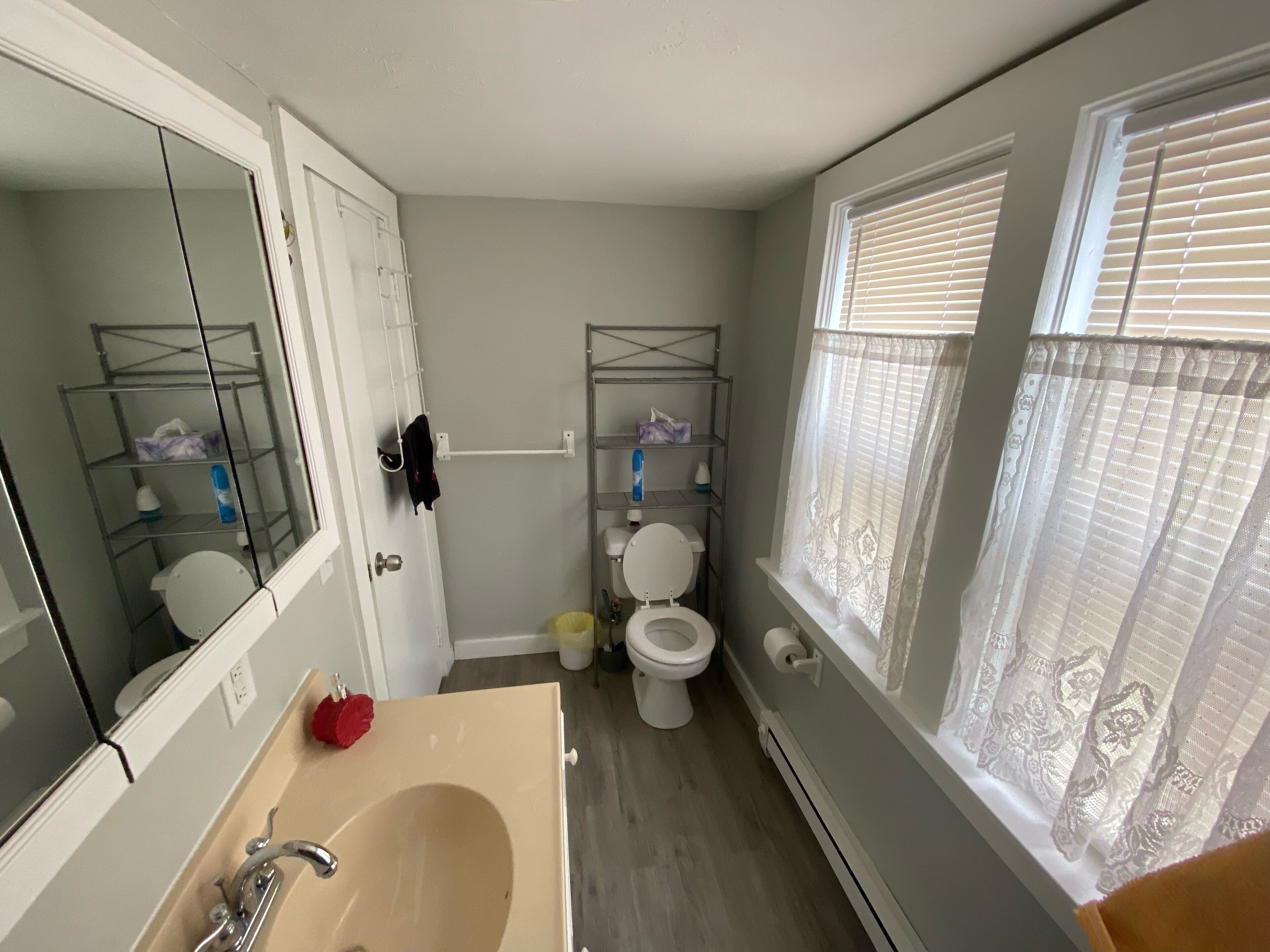 A bathroom with a large mirror, a sink, a toilet, and a window with blinds.