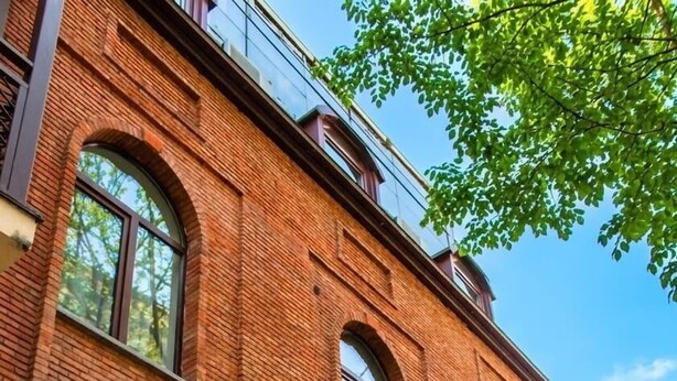 Un bâtiment en briques doté de grandes fenêtres, d’une porte et d’un petit jardinier avec des fleurs.