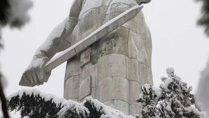 Une statue représentant une figure tenant une épée, entourée d’arbres couverts de neige.