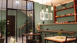 Un espace repas comprenant un escalier, une table en bois, des chaises, des luminaires suspendus et une étagère où sont disposés divers objets.