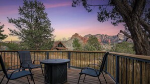 Une terrasse en bois avec deux chaises et une table, d’où l’on peut admirer un paysage montagneux avec une maison en arrière-plan.