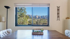 Un coin repas comprenant une grande table, deux chaises, une fenêtre donnant sur les montagnes et un élément décoratif mural.