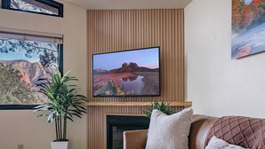 Un salon doté d’un téléviseur à écran plat fixé au-dessus d’une cheminée, d’un canapé avec des coussins, d’une plante en pot et d’une fenêtre offrant une vue sur un canyon.