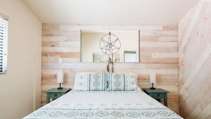 Une chambre avec un mur recouvert de lattes de bois, un lit avec une literie à motifs, deux tables de chevet avec des lampes et un attrape-rêves accroché au mur.