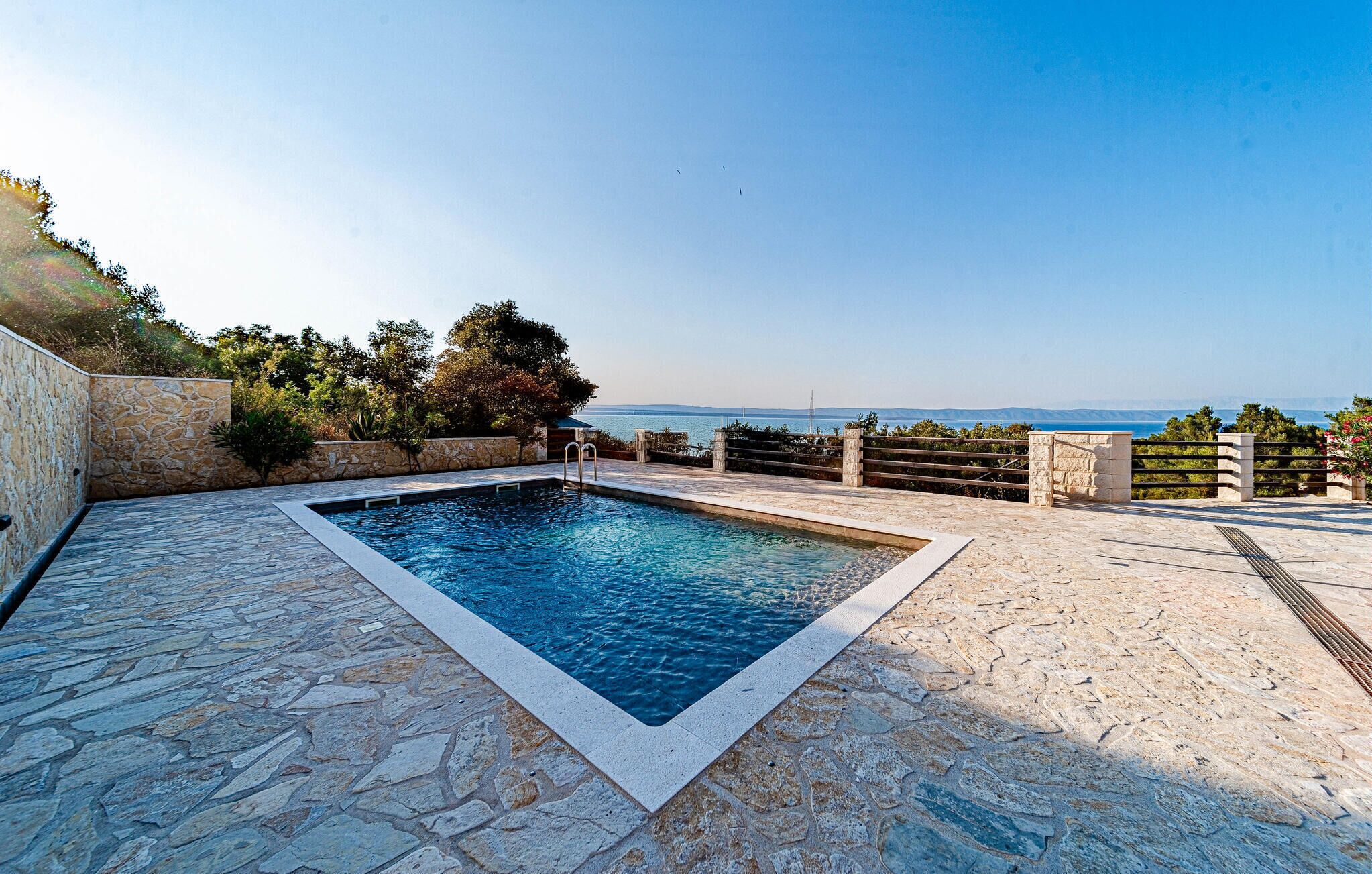 A rectangular swimming pool with stone tiles, surrounded by a stone deck and a low stone wall.