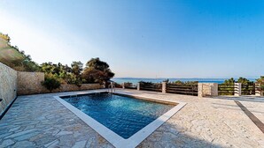 A rectangular swimming pool with stone tiles, surrounded by a stone deck and a low stone wall.