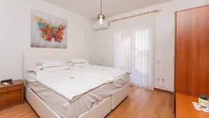 A bedroom with a bed, a nightstand, a wooden wardrobe, a window with sheer curtains, and a wall-mounted air conditioner. - 1 bedroom beautiful apartment in Biograd na Moru (Biograd na Moru)
