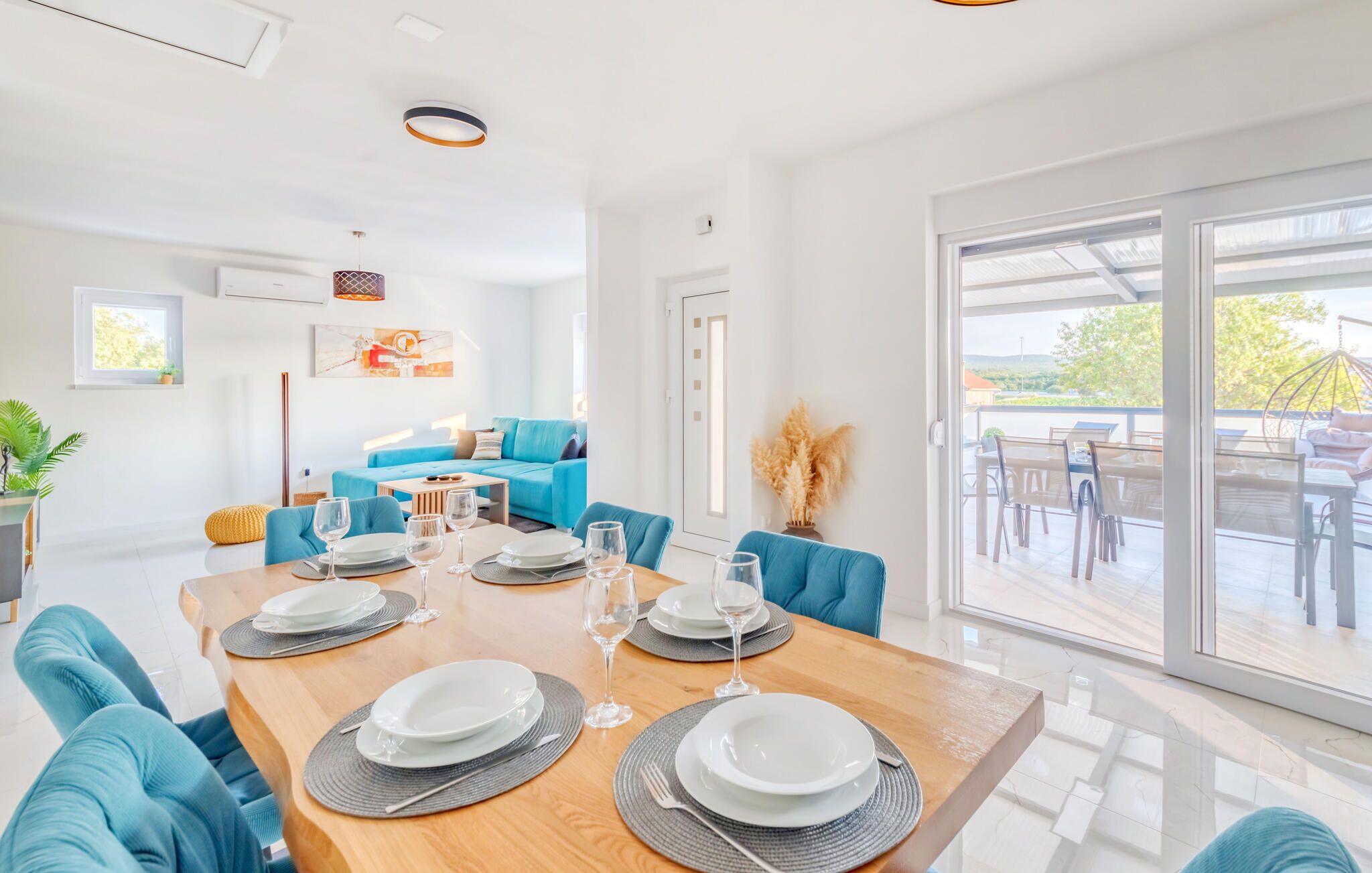 A modern dining area with a wooden table set for four, blue upholstered chairs, and a view of an outdoor patio with a glass door.