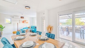 Et moderne spiseområde med et træbord dækket til fire personer, bløde blå stole og udsigt til en udendørs terrasse med en glasdør.