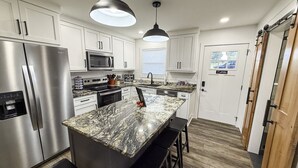 A modern kitchen with white cabinets, stainless steel appliances, a granite countertop island, and black bar stools.