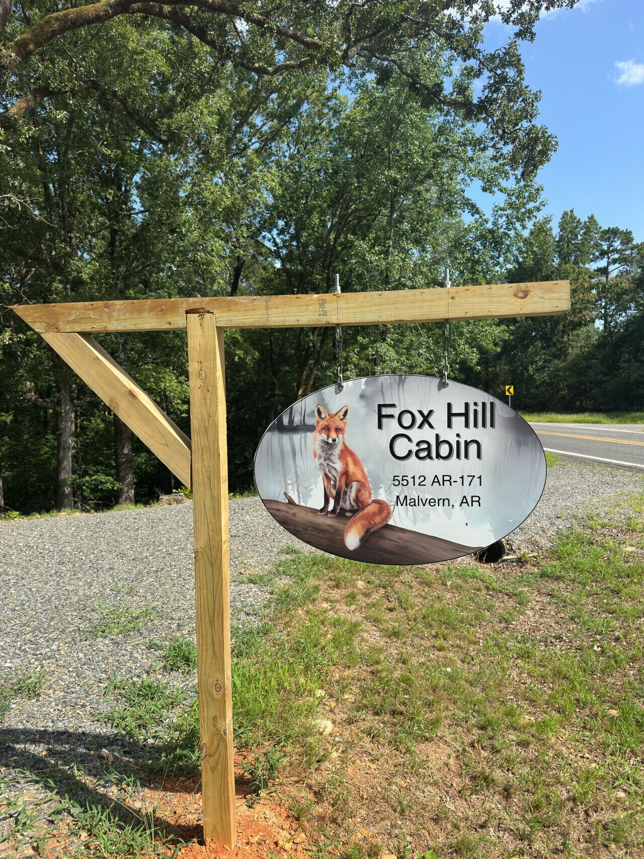 Ein Holzschild mit einer Fuchs-Illustration und dem Text Fox Hill Cabin, Malvern, AR, inklusive einer Telefonnummer.