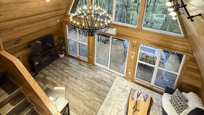 A spacious loft-style room with a large window, a chandelier, and a wooden staircase.