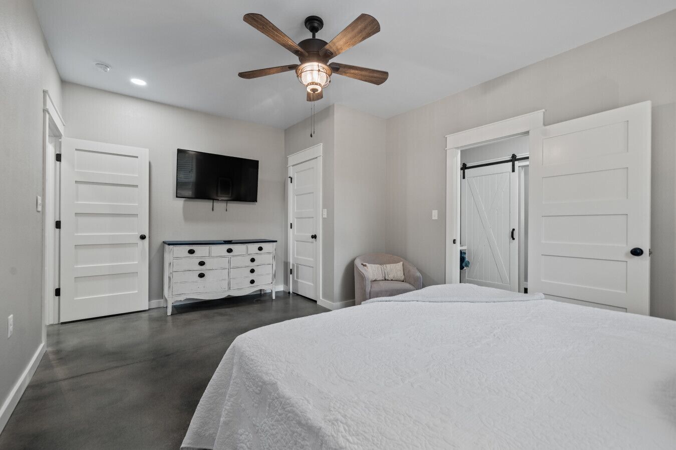 A bedroom with a bed, a ceiling fan, a dresser, a TV, and two doors.