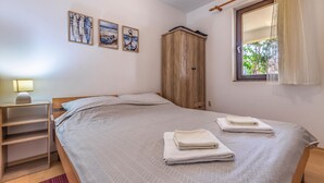 A bedroom with a bed, a wooden wardrobe, a nightstand with a lamp, and three wall-mounted paintings. - 1 bedroom amazing apartment in Medulin (Medulin)