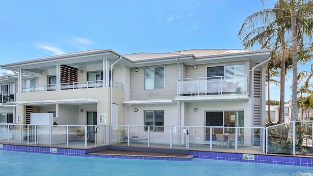 Un edificio residencial de varios pisos con balcones, piscina y palmeras.