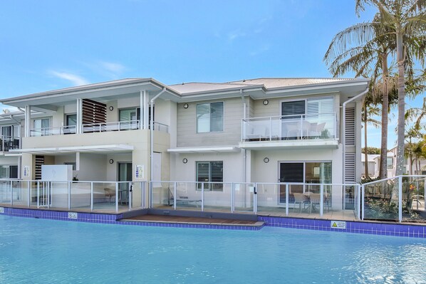 Un edificio residencial de varios pisos con balcones, piscina y palmeras.