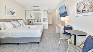 Una habitación de hotel con cama, escritorio, silla, televisor y espejo.