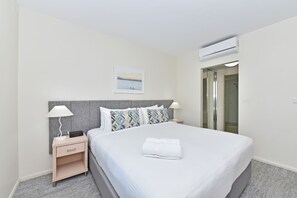 Una camera d'albergo con un letto, un comodino, una lampada, un condizionatore d'aria a muro e un quadro incorniciato.