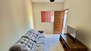 A living room with a grey sectional sofa, a wooden TV stand, and a tiled floor. - House with Pool and Barbecue (Santa Mônica Guarapari)