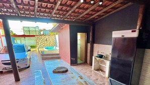 An outdoor kitchen area with a table, a refrigerator, and a car parked nearby. - House with Pool and Barbecue (Santa Mônica Guarapari)