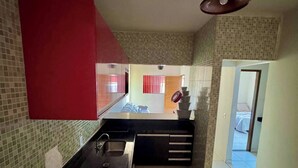 A kitchen with a red cabinet, a sink, and a tiled backsplash. There is a staircase leading to an upper level. - House with Pool and Barbecue (Santa Mônica Guarapari)