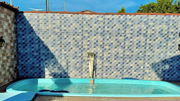 A swimming pool with a tiled wall and a wooden deck. - House with Pool and Barbecue (Santa Mônica Guarapari)