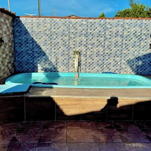 A swimming pool with a tiled wall and a wooden deck. - House with a pool and barbecue (Santa Mônica Guarapari)