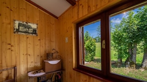 En stuga med träpanel, ett fönster, ett litet bord med en korg och en stol.