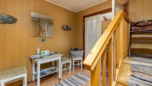 Ett rum med träpanel på väggarna, ett vitt bord, en spegel, en liten pall, en matta och en trappa.