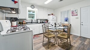 Une cuisine de taille réduite avec des meubles blancs, une cuisinière à gaz, une table à manger avec des chaises et une horloge au mur.