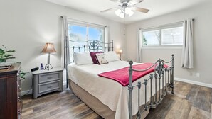 Une chambre à coucher avec un lit, des tables de chevet, un ventilateur de plafond et des fenêtres.