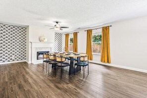A dining area with a wooden table and chairs, a ceiling fan, and a fireplace. - The Grove of Calm (Locust Grove)