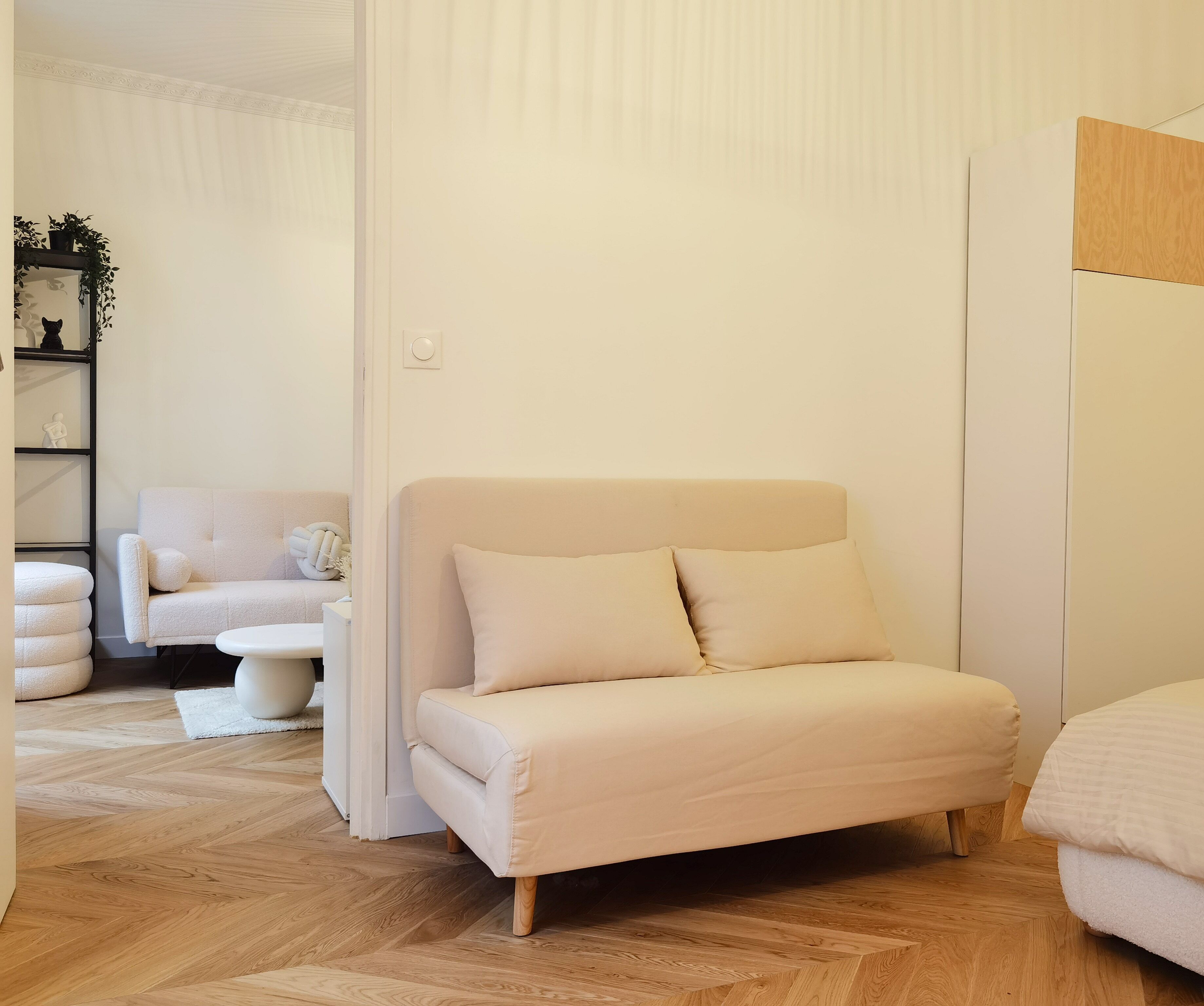 A modern bedroom with a large bed, a small sofa, and a wooden floor.