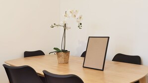 Une table ronde en bois, entourée de chaises noires, un pot de fleurs en osier et un objet encadré posé sur la table.