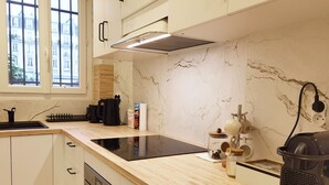 Une cuisine moderne dotée d’une plaque de cuisson à induction noire, de meubles blancs, d’un four encastré et d’une fenêtre offrant une vue sur les bâtiments.