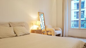 Une chambre d’hôtel avec un grand lit, une table de chevet avec une lampe, une chaise et une fenêtre donnant sur des immeubles.