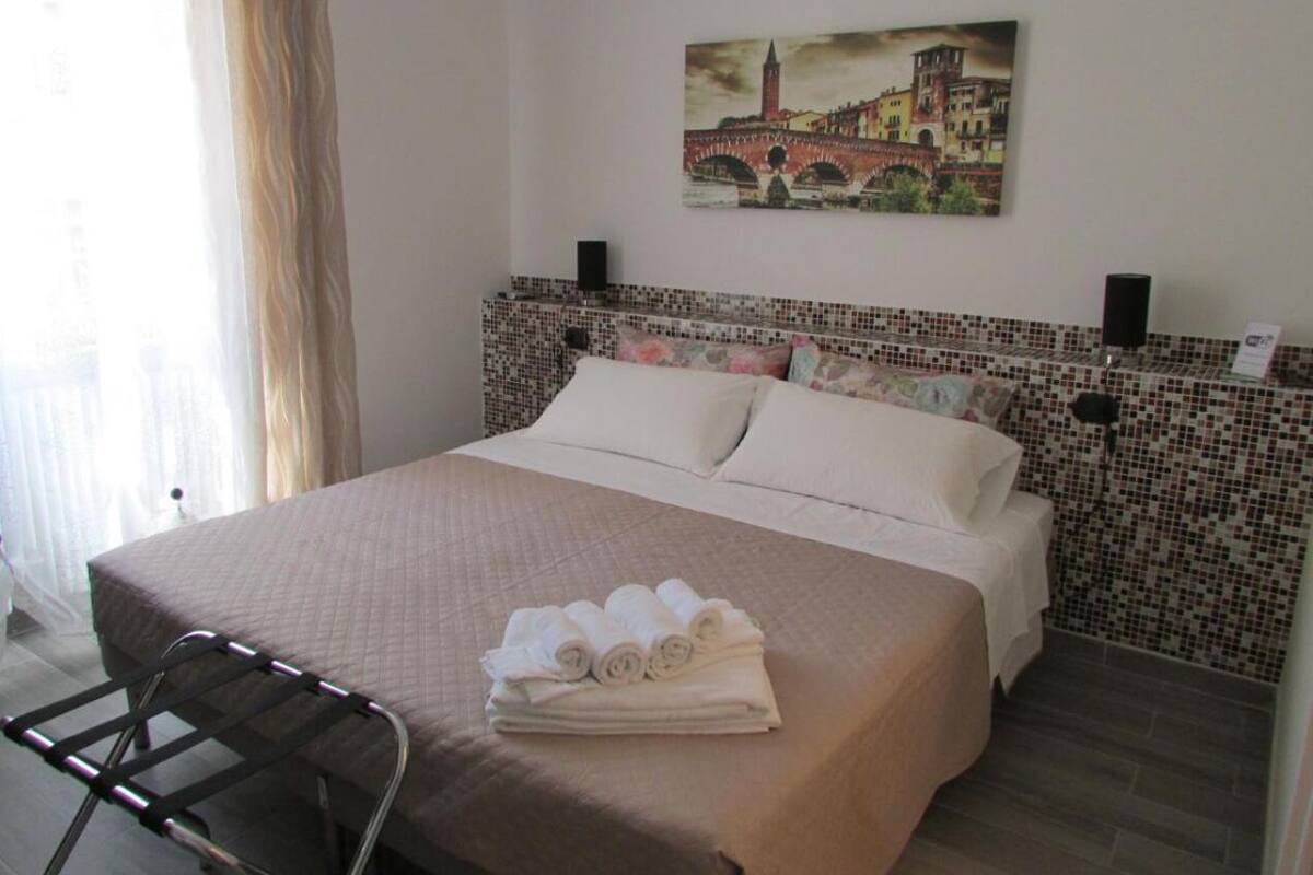 A hotel room with a bed, a chair, a painting on the wall, and a tiled headboard.