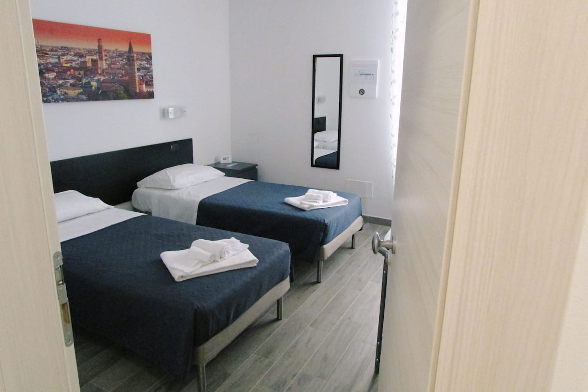 A hotel room with two beds, a nightstand, a mirror, and a cityscape painting on the wall.