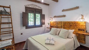 A bedroom with a wooden headboard, a bed with white linens, a ladder, and a window with shutters. - Cortijo Miraflores Arenas by Ruralidays (Málaga)
