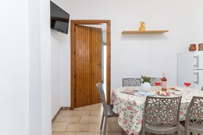 Un coin repas avec une porte en bois, une table recouverte d’une nappe à motifs floraux et un buffet blanc avec une étagère au-dessus.