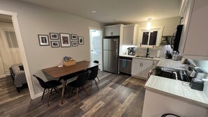 Een moderne keuken met witte kastjes, een ingebouwde oven, en een eethoek met een houten tafel en stoelen.