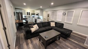 Een moderne woonkamer met een modulaire bank, een salontafel en een eethoek, met een keuken op de achtergrond.